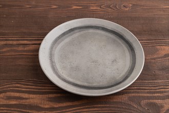Empty gray ceramic plate on brown wooden background. Side view, copy space