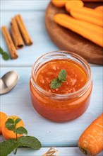 Carrot jam with cinnamon in glass jar on blue wooden background. Side view, close up, selective