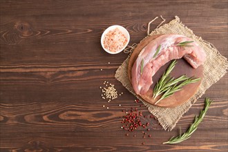 Raw pork with herbs and spices on a wooden cutting board on a brown wooden background. Top view,