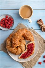 Homemade sweet bun with raspberry jam and cup of coffee on a blue wooden background and linen