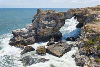 Picturesque rock arch on the coast with foamy waves, summer blue sky and signs of erosion, stone
