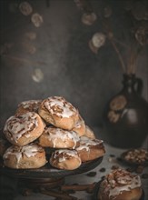 Homemade cinnamon buns surrounded by nuts, sultanas and cinnamon sticks on a dark background
