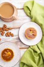 Sweet tartlets with almonds and caramel cream with cup of coffee on a white wooden background and