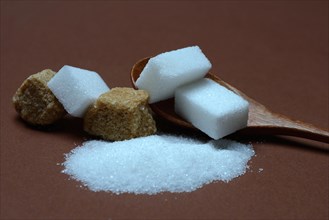 Granulated sugar and sugar cubes in spoons, brown raw sugar