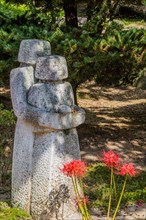 Stone carved statue of two figures behind tiger lily flowers in mountain park in Gimje-si, South