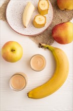 Baby puree with fruits mix, apple, banana infant formula in glass jar on white wooden background.