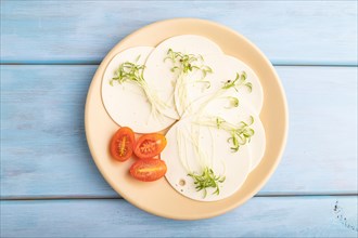 White cheese with tomatoes and cilantro microgreen on blue wooden background. top view, flat lay,