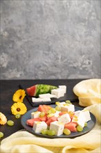 Vegetarian salad with watermelon, feta cheese, and grapes on blue ceramic plate on black concrete