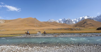 Riders on horses on the river bank, mountain landscape with yellow meadows and river Kol Suu,