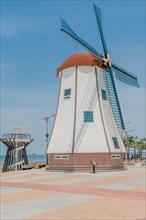 Windmill at Chunjangdae Beach on sunny day with hazy blue sky in background in South Korea
