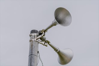 Large metal loud speakers used for emergency warnings mounted on top of metal pole against gray sky