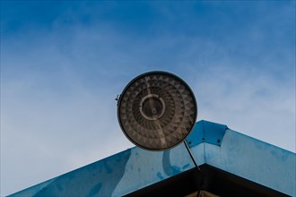 Large street light with a metal shade mounted to the roof of a metal building with blue sky in the