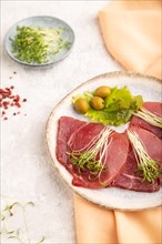 Slices of smoked salted meat with cilantro microgreen on gray concrete background and orange