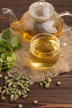 Green oolong tea with herbs in glass on brown wooden background and linen textile. Healthy drink