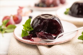 Black currant and grapes jelly on white wooden background and linen textile. side view, close up,