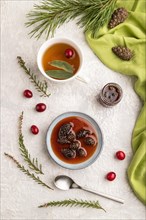 Pine cone jam with herbal tea on gray concrete background and green linen textile. Top view, flat