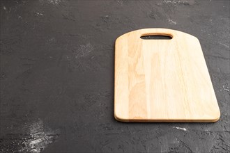 Empty rectangular wooden cutting board on black concrete background. Side view, copy space