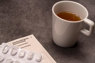 A cup of tea next to medication and a certificate of incapacity for work on a grey background