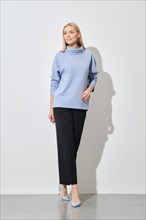 A modern fashion model poses in a relaxed stance, wearing a stylish blue sweater paired with