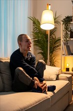 Vertical photo of a sad disabled man sitting on the sofa alone at home