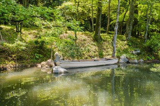 Wooden row boat in water at river bank in Shukkeien gardens in Hiroshima, Japan, Asia