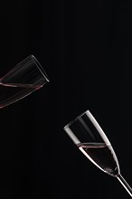 Two half-filled champagne glasses tilted towards each other against a black background
