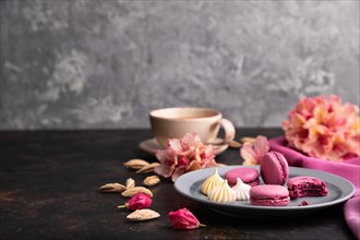 Purple macarons or macaroons cakes with cup of coffee on a black concrete background and pink