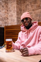 Vertical photo of a stylish african young man drinking beer in a bar