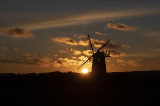 Windmill silhouetted at sunset with a red sky and clouds, Burnham Ovary Staithe, Norfolk, England,