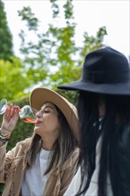 Vertical image of a relaxed young woman drinking a glass of wine with a friend in the park