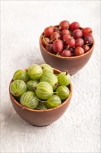 Fresh red and green gooseberry in clay bowl on gray concrete background. side view, close up