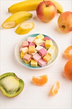 Various fruit jelly chewing candies on plate on white wooden background. apple, banana, tangerine,