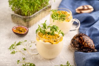 Yogurt with passionfruit and marigold microgreen in glass on gray concrete background with blue