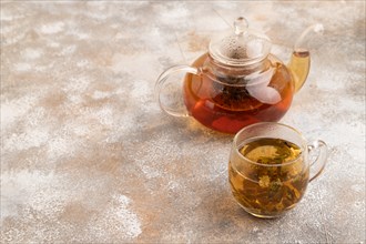 Red tea with herbs in glass teapot on brown concrete background. Healthy drink concept. Side view,