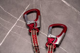 Two red carabiners with safety ropes on a grey stone-like background, studio photo, Germany, Europe