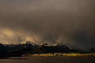 Lake Hopfensee with stormy sky in soft morning light and Allgaeu mountains in the background,