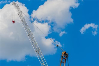 Arm of construction crane against white puffy clouds in a clear blue sky
