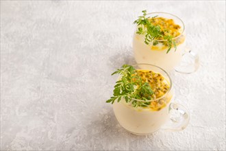 Yogurt with passionfruit and marigold microgreen in glass on gray concrete background. Side view,