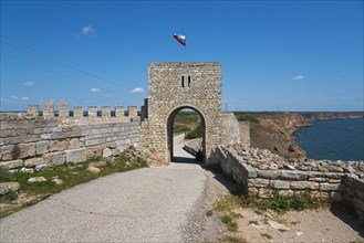 Stone fortress walls with arcade entrance and waving flag on a sunny day, fortress ruins, Cape
