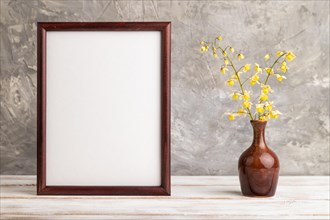 Wooden frame with yellow barrenwort flowers in ceramic vase on gray concrete background. side view,