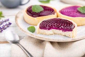 Sweet tartlets with jelly and milk cream with cup of coffee on a white wooden background and linen