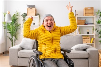 Portrait of a happy disabled man in wheelchair raising hands in joy celebrating in the living room