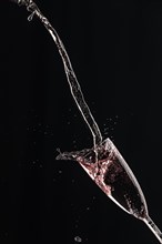 Rose champagne pours in an arc into a champagne glass on a black background