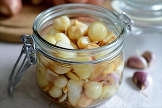An open preserving jar full of pickled shallots and garlic cloves on a table, AI generated, AI