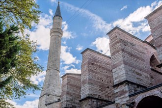 Minaret towering above external wall of mosque under cloudy blue sky in Istanbul, Turkiye