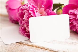 White business card with pink peony flowers on white wooden background. side view, copy space,