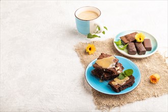 Chocolate brownie with caramel sauce with a cup of coffee on gray concrete background and linen