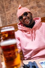 Vertical photo of a cool african man toasting with beer in a bar