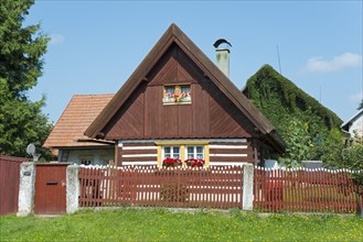 Small cottage with a red roof and white shutters, surrounded by a garden and a wooden fence, Old