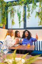 Vertical shot of three female friends taking selfie with mobile phone while drinking coffee in a
